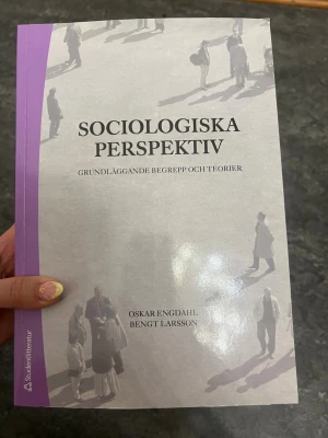 Sociologiska perspektiv kursbok - Kurslitteratur: 'Sociologiska perspektiv – Grundläggande begrepp och teorier' av Oskar Engdahl och Bengt Larsson. Boken har ett lila och vitt omslag med silhuetter av människor. Perfekt för dig som pluggar sociologi eller samhällsvetenskap.