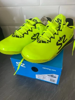 Salming S2 neongula inomhusskor - Säljer ett par Salming S2 inomhusskor i en riktigt snygg neongul färg med svarta detaljer och logga. Skorna har snörning och en slitstark sula som passar perfekt för snabba sporter inomhus. Materialet är syntet och mesh för bra ventilation.