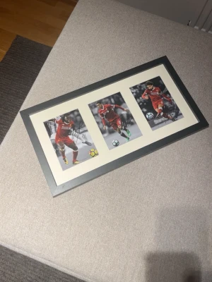 Inramade fotbollsbilder Liverpool - Snygg tavla med tre inramade fotbollsbilder på Mane, Firmino och Salah - spelare i Liverpool FC:s röda matchställ. Bilderna är signerade av spelarna. Svart ram och vit passepartout ger en stilren look, perfekt för fotbollsälskare och samlare.