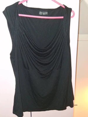 Svart ärmlös topp från Bodyflirt - Snygg svart ärmlös topp från Bodyflirt med draperad framsida och mjukt fall. Perfekt till jeans eller kjol för en stilren look. Tillverkad i ett stretchigt material som känns bekvämt mot huden.