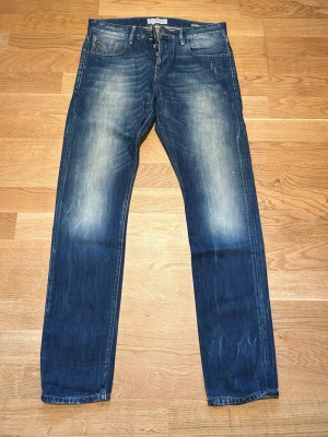 Mörkblå raka jeans med slitningar - Snygga blå slim fit jeans från Scotch & Soda (modell Ralston). Slitna detaljer och ljusa partier på låren från fabrik. Klassisk femficksmodell med knappgylf och raka ben. Perfekta för en avslappnad och trendig look. Strl 30/32