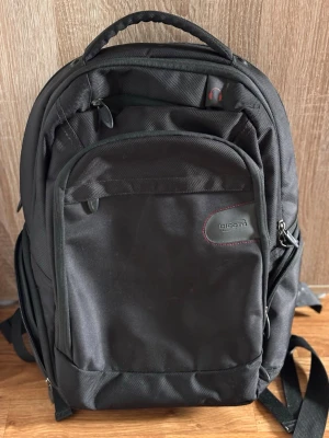 Svart ryggsäck från Dicota - Snygg svart ryggsäck från Dicota med flera fack och vadderade axelremmar. Tillverkad i slitstarkt tyg och har praktiskt bärhandtag upptill. Perfekt för laptop och skolgrejer, med smarta innerfack och dragkedjor. Enkel och stilren design med diskret logga.