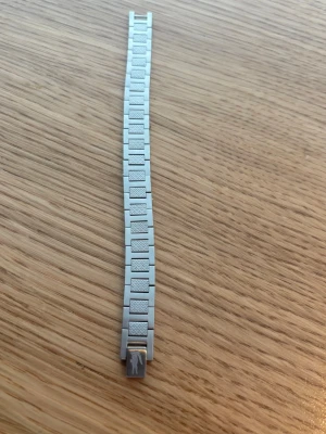 Silverfärgat länkarmband från Pilgrim - Snyggt armband i silverfärgad metall med rektangulära länkar och diskret mönster på varje länk. Klassisk design med Pilgrim-logga på låset. Perfekt accessoar för en stilren look.