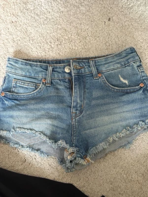 Blå jeansshorts med fransig kant - Säljer ett par klassiska blå jeansshorts med fransig kant och slitningar. 