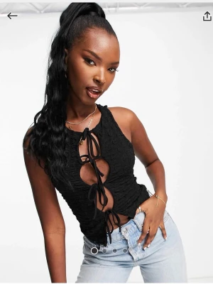 Svart snörad croppad linnetopp - Trendig svart linnetopp med snörning framtill och croppad passform. Toppen är ärmlös och har flera knytningar som ger en edgy look. Köpt på ASOS från Motel, använd 1 gång.