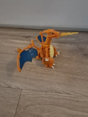 Charizard byggsats Pokémon leksak - Säljer en cool Charizard byggsats från Pokémon. Figuren är orange med blå vingar och gul mage, och kan skjuta eld ur munnen. Tillverkad i plast och perfekt för samlare eller Pokémon-fans som gillar att bygga och leka. Den kommer utan manual, och kommer uppbyggd. Vingarna och elden i munnen kan åka av i paketet.