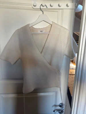 Beige/vit omlottopp från Gina tricot - Säljer en supermjuk beige omlottopp från Gina med korta ärmar och knytband i sidan.