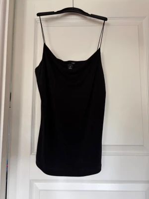 Svart, glittrigt partylinne - Svart, glittrigt partylinne med smala axelband och strävt material. H&M, storlek M