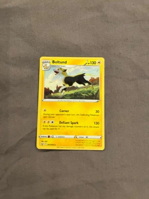 Pokémonkort Boltund - Säljer ett Pokémonkort med Boltund-motivet. Kortet är guldfärgat med svart och vitt motiv, och har en klassisk rektangulär form. Text och illustration är tryckt på papper/kartong. Perfekt för samlare eller Pokémonfans.