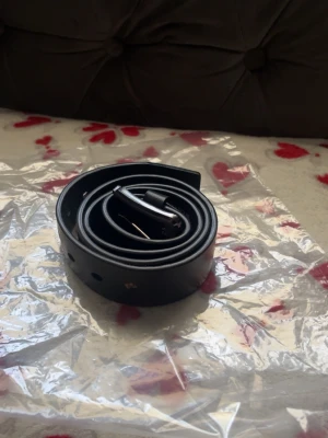 Svart klassiskt skärp i skinn - Stilrent svart bälte i skinn med silverfärgat spänne. Perfekt till jeans eller kostymbyxor. Enkel design utan mönster och med justerbara hål för bästa passform.