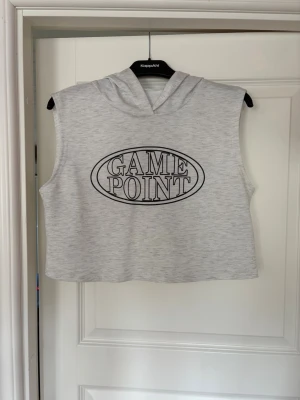Sportig croppad ärmlös hoodie - Grå croppad hoodie utan ärmar. Tryck 'GAME POINT' framtill och huva baktill. Storlek S.
