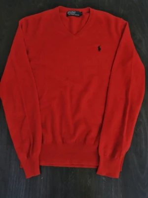 Röd tröja från Polo Ralph Lauren - Säljer en röd v-ringad tröja från Polo Ralph Lauren med klassisk broderad logga på bröstet. Tröjan har lång ärm och är tillverkad i mjuk ull som känns skön mot huden. Perfekt för dig som gillar stilrena och tidlösa plagg. Axelbredd: 43cm / Längd: 63cm. Nypris: 725kr / Mitt pris: 159kr