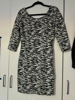 Svartvit mönstrad klänning från GUESS - En svartvit kortklänning med abstrakt mönster och trekvartsärm från GUESS. Klänningen har en v-ringad hals och är figurnära med normal passning och fin logga i metall. I storlek 38/M.