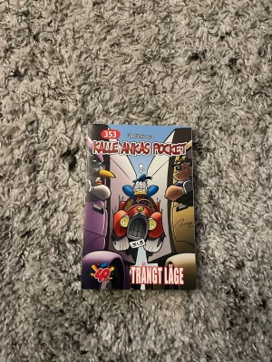 Kalle Ankas Pocket 353 Trångt Läge - Kalle Ankas Pocket nummer 353, 'Trångt Läge', är en färgglad pocketbok med tecknade serier om Kalle Anka och hans vänner. Omslaget är illustrerat med Kalle i en bil och typiska Disney-karaktärer. Perfekt för dig som gillar humor och äventyr i serieformat.