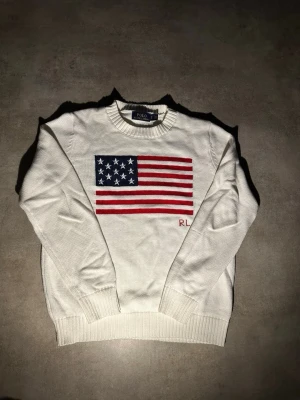 Vit stickad tröja Polo Ralph Lauren - Vit stickad tröja från Polo Ralph Lauren med amerikansk flagga i blått, rött och vitt på bröstet samt RL-broderi. Den är i ny kondition och passar 170-175cm 