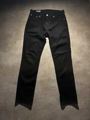 Svarta Levi's skinny jeans - Säljer ett par svarta skinny jeans från Levi's med klassisk femficksdesign och silverfärgade nitar. Jeansen har en smal passform och är tillverkade i ett mjukt bomullsmaterial med lite stretch. Perfekta för en clean och stilren look.