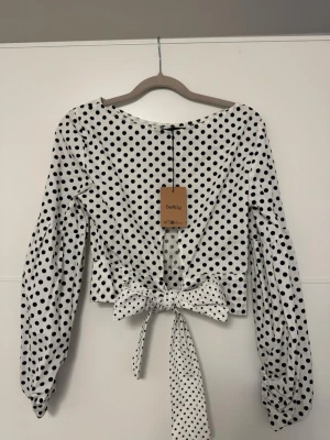 Vit prickig topp med knytband - Trendig vit topp / blus från Zara med svarta prickar och långa puffärmar. Toppen har ett brett knytband i midjan som ger en snygg siluett och en rundad halsringning. Perfekt för dig som gillar retrovibbar och vill sticka ut lite extra. Lite ”skjortmaterial” på den😍