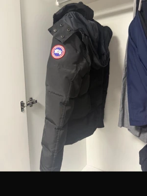 Svart dunjacka från Canada Goose - Säljer en svart dunjacka från Canada Goose med klassisk patch på ärmen. Jackan har hög krage, dragkedja och knappar framtill samt flera fickor. Perfekt för kalla vinterdagar och riktigt varm tack vare dunfyllningen. JACKAN ÄR ÄKTA,KOM PRIVAT OM DU ÄR INTRESSERAD 
