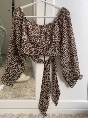Leopardmönstrad omlottopp med knyt - Trendig leopardmönstrad omlottopp med långa, luftiga ärmar och knyt framtill. Toppen har en croppad passform och är tillverkad i ett lätt, transparent material som ger en cool och luftig känsla.