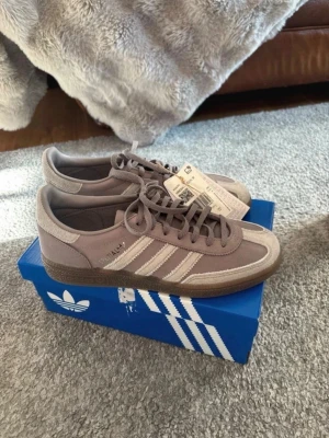 Adidas Samba OG grå sneakers - Säljer ett par Adidas  spezial sneakers i grått mocka och läder med klassiska vita stripes på sidan. Skorna har gummisula och låg profil, perfekt för en clean och stilren look. Ikonisk Adidas-logga på plösen och insidan. Levereras i originalkartong. Storlek 39 1/3
