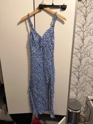 Blå blommig långklänning från newyorker eller Sister - Supersöt långklänning från newyorker eller sister i blått och vitt med blommigt mönster. Klänningen har smala axelband, v-ringad front och en slits på sidan som ger en snygg touch. Perfekt för sommarens alla äventyr!