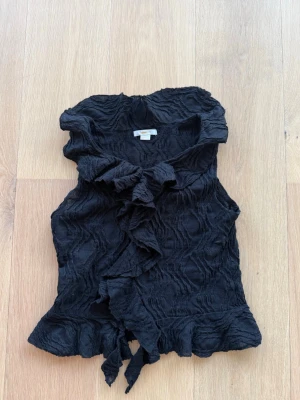 Svart volangblus från Gina Tricot - Svart kortärmad blus från Gina tricot i storlek 158-164cm säljs så den är för liten. Har en fläck på insidan av en volang som visas på sista sidan. 