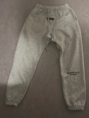 Grå Essentials mjukisbyxor - Snygga grå mjukisbyxor från Essentials med tryck på benet och elastisk midja med dragsnöre. Byxorna har ribbade benslut, sidofickor och en bakficka. Perfekta för chill och streetwear-stil.