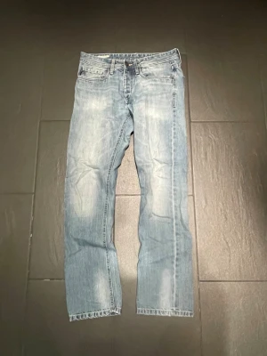 Ljusblå raka jeans från jacka and jonses - Säljer ett par ljusblå jeans från jack and jones med rak passform och slitna detaljer vid benslut. Jeansen har klassisk femficksmodell, dragkedjegylf och är tillverkade i denim. Perfekta för en avslappnad och trendig look. Mfg originals