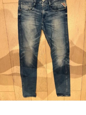 Replay Anbass jeans - Snygga blå slim fit jeans från Replay med slitna detaljer och klassisk femficksdesign. Jeansen har en något tvättad look och smal passform som sitter tajt längs benen. Perfekta för en trendig och avslappnad stil. Längd 34 midja 31