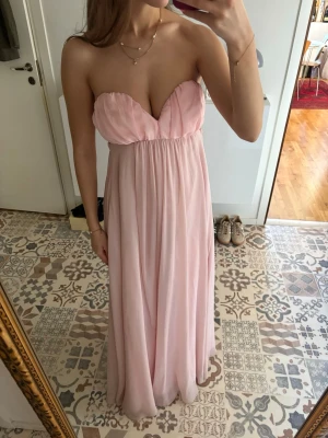 Ljusrosa axelbandslös långklänning - En supersöt ljusrosa långklänning perfekt för bal! Klänningen har axelbandslös design, öppwn rygg och en flowy passform. Jag är 168 cm och klänningen går till marken på mig. Passar både storlek S och M då man knyter åt i ryggen och midjebandet har resår. 