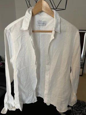 Vit linneskjorta från Pier One - Klassisk vit skjorta från Pier One i svalt linne. Skjortan har lång ärm, krage och knappar framtill. Perfekt för en clean och stilren look, lätt att matcha med olika outfits.