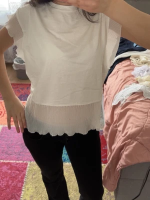 Vit blus med plisserade detaljer - Snygg vit blus från Anna Field med plisserade volangdetaljer på ärmar och nederkant. Rak passform och rund halsringning. Perfekt för dig som gillar en stilren look med en twist.