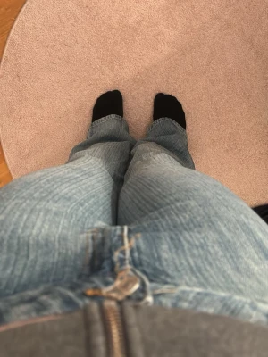 Blå bootcut jeans med slitningar - Säljer ett par ljusblå bootcut jeans med snygga slitningar och klassisk femficksmodell. Jeansen har dragkedjegylf och är tillverkade i mjuk denim. Perfekta för en avslappnad och trendig look. Pris kan alltid diskuteras