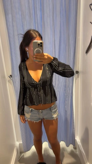 Svart blus med paljettdetaljer från Subdued - Snygg svart blus med silver paljetter och knytning i ryggen, perfekt för festligheter. Blusen är från Subdued och är köpt i Thailand och aldrig använd, prislapp finns kvar.