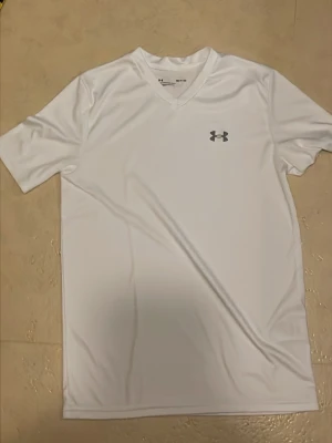 Vit sport-tshirt från Under Armour - Säljer en vit sport-tshirt från Under Armour med v-ringning och korta ärmar. Perfekt för gymmet 