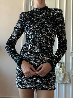 Svart glittrig paljettklänning - Supersnygg svart/silvrig kort paljettklänning med lång ärm och öppen rygg.