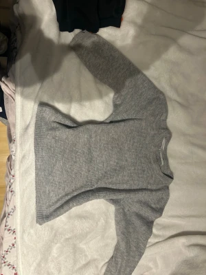 Grå ribbstickad tröja Gina Tricot med puffarmar  - Mysig grå stickad tröja från Gina Tricot med ribbstickat mönster. Tröjan har rund halsringning och långa ärmar, perfekt för lager-på-lager. Enkel och stilren design som passar till det mesta.