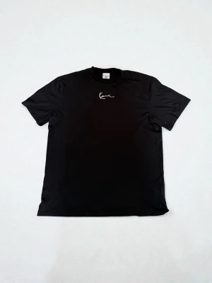 Svart Karl Kani t-shirt i bomull - Snygg svart t-shirt från Karl Kani med vit broderad logga på bröstet. Den är ifrån 2000-talet alltså vintage. Klassisk rund hals och korta ärmar. Tillverkad i mjuk bomull som känns skön mot huden. Perfekt för en avslappnad streetwear-look.