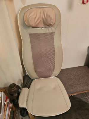 Massagekudde med fjärrkontroll - Beige massagekudde för rygg och nacke med tillhörande fjärrkontroll. Kudden har mesh-tyg i mitten och konstläder runtom. Flera massageinställningar som shiatsu, värme och rullning kan styras via fjärrkontrollen. Perfekt för att slappna av hemma.