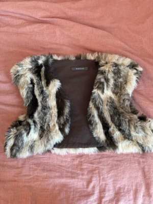 Söt päls bolero - Säljer en fluffig päls bolero i bruna, beige och svarta toner. Perfekt för att lyfta din outfit med en trendig touch och cool struktur. Står strl ”one size” men passar mig som vanligtvis har S! Fuskpäls!