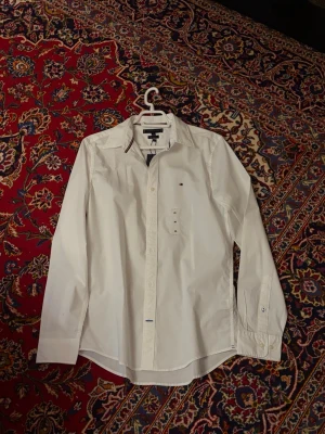 Vit Tommy Hilfiger Skjorta  - Helt sprillans ny skjorta, säljs pga missnöjd brorsa.., säljer den för mycket billigare än vad den är på marknaden och den är såklart äkta. Kommer med förpackningen också!
