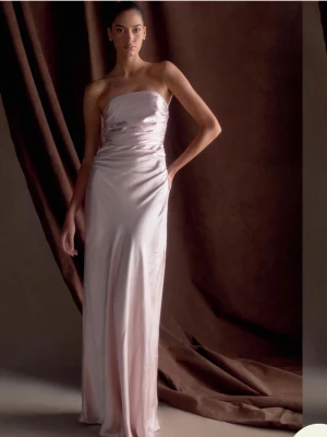 Rosa balklänning meshki - Säljer en elegant axelbandslös balklänning i ljusrosa satin. Klänningen har en figurnära passform med lätt rynkade detaljer vid midjan. Helt ny med prislapp!🩷
