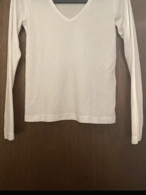 Vit långärmad topp med V-ringning - En stilren vit långärmad topp med V-ringning. Enkel och clean design som passar perfekt till jeans eller kjol. Tillverkad i ett mjukt och stretchigt material för en bekväm känsla hela dagen.