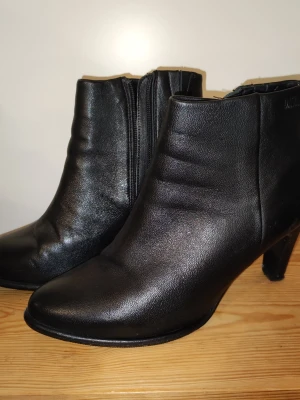 Svarta stövletter i skinn med klack - Snygga svarta stövletter i äkta skinn med smal klack och dragkedja på sidan. Klassisk design som passar till många olika outfits. Perfekta för dig som vill ha en stilren och tidlös look.