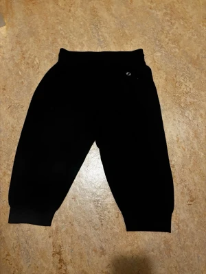 Svarta mjukisbyxor med dragsko - Svarta mjukisbyxor från Stadium med resår i midjan och dragsko för skön passform. Byxorna har ribbade muddar vid bensluten och en liten logga på höften. Perfekta för chill eller träning. Dom går precis under knäna så är 2/3.💖