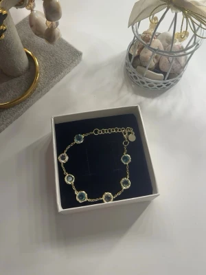 Guldarmband Snö of Sweden - Snyggt armband i guldton med runda blå och vita pärlor infattade i länkar. Justerbar längd med karbinlås och liten rund bricka vid låset. Perfekt för dig som gillar stilrena och eleganta accessoarer med en touch av färg.