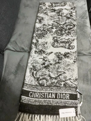 Christian Dior halsduk - Lyxig halsduk från Christian Dior i svartvitt med ikoniskt toile de Jouy-mönster och fransar i ändarna. Märkets logga är invävd längs kanten. Perfekt accessoar för att lyfta din outfit med exklusiv känsla. Säljas så snabbt som möjligt + pris kan diskuteras !!!