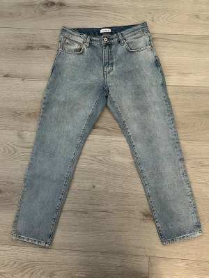 Ljusblå raka jeans från Woodbird - Säljer ett par ljusblå jeans från Woodbird med rak passform och klassisk femficksdesign. Jeansen har normal midja, knappgylf och är tillverkade i denim av bomull. Perfekta för en avslappnad och trendig look.