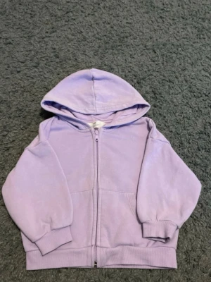 Ljuslila hoodie från H&M - Snygg ljuslila hoodie från H&M med dragkedja framtill och stor huva. Tillverkad i mjuk bomullsblandning och har ribbade muddar vid ärmar och nederkant. Perfekt för en chill och avslappnad stil.