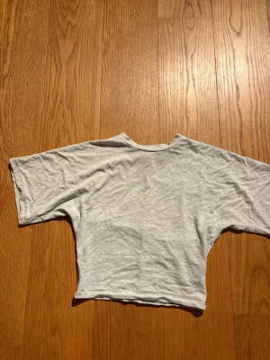 Ljusgrå croppad t-shirt - En enkel ljusgrå croppad t-shirt med korta ärmar och rund hals. T-shirten har en rak passform och är tillverkad i mjuk bomull, perfekt för en avslappnad och stilren look.